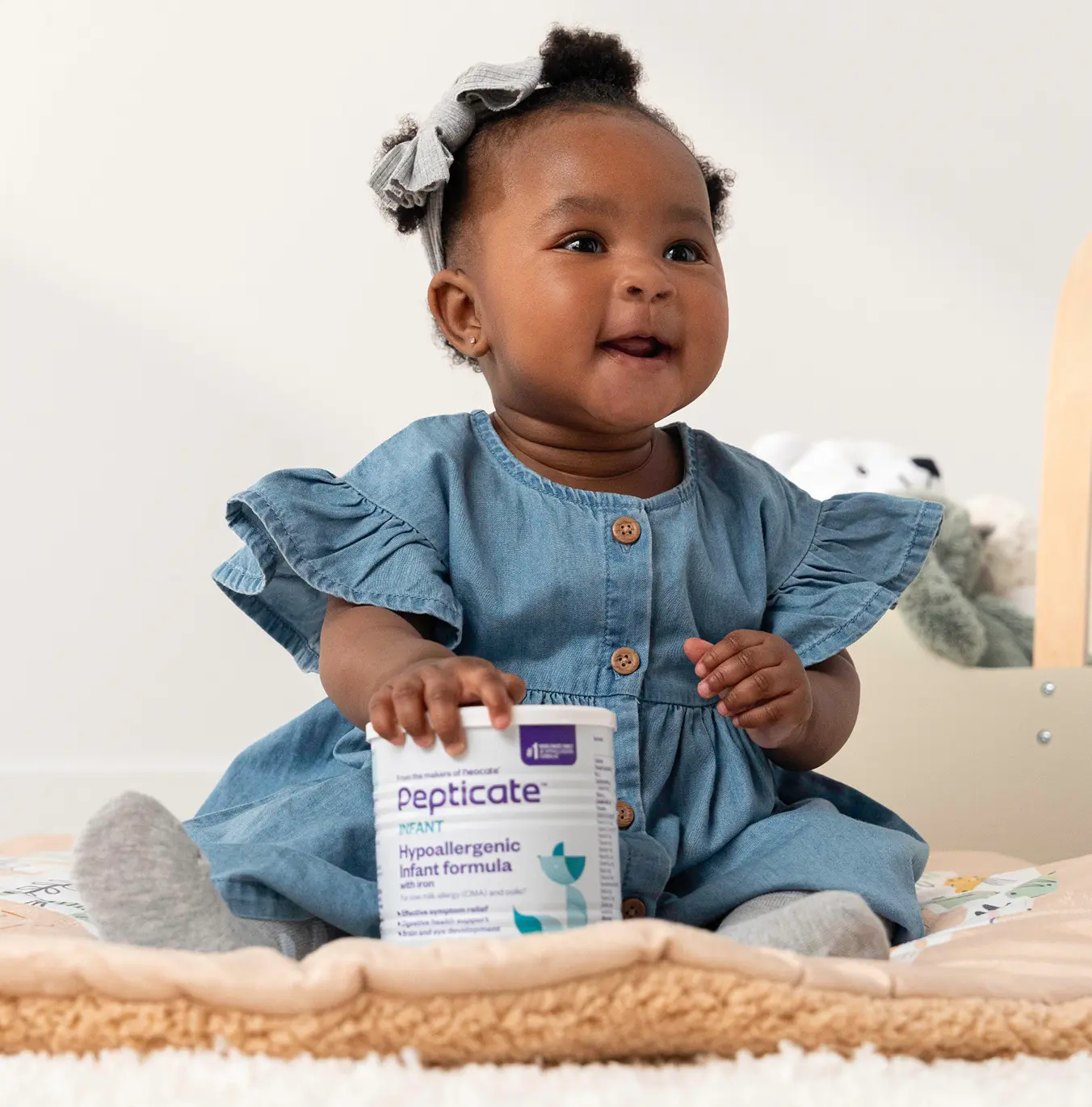 A baby sitting with a can of Pepticate formula