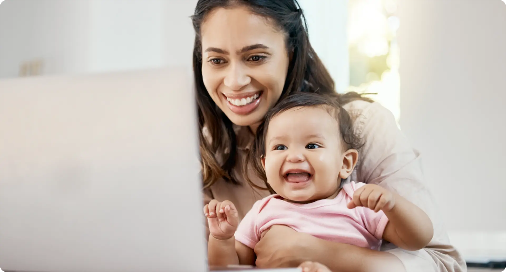 A mother holding a baby and using a laptop.